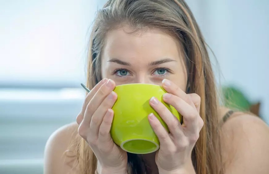 woman drinking out of a large green mug